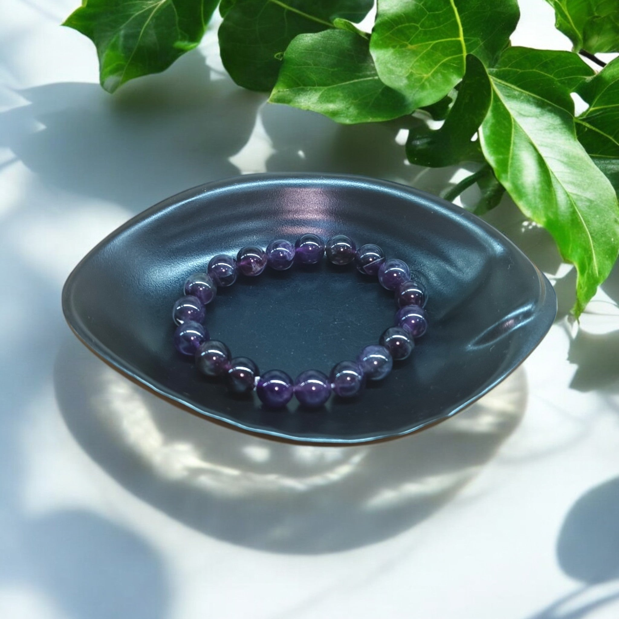 "Natural Amethyst elastic bracelet with 10 mm purple beads on Black dish and green leaves in background – crystal jewellery for calm and clarity" 