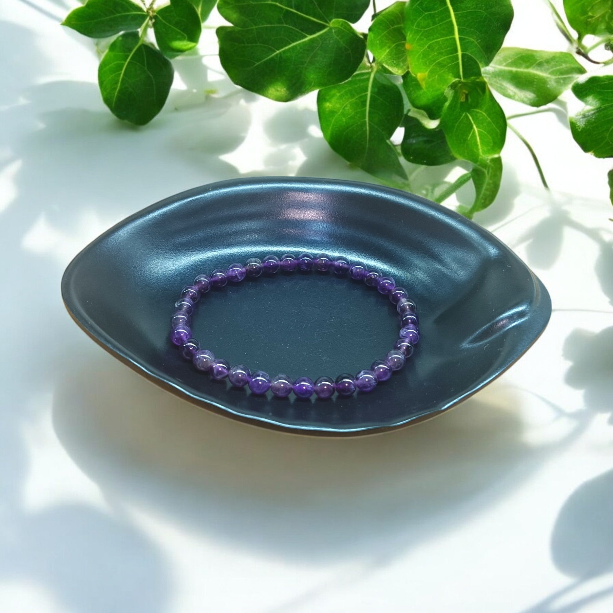 "Natural Amethyst elastic bracelet with 6 mm purple beads on Black dish and green leaves in background – crystal jewelry for calm and clarity" 