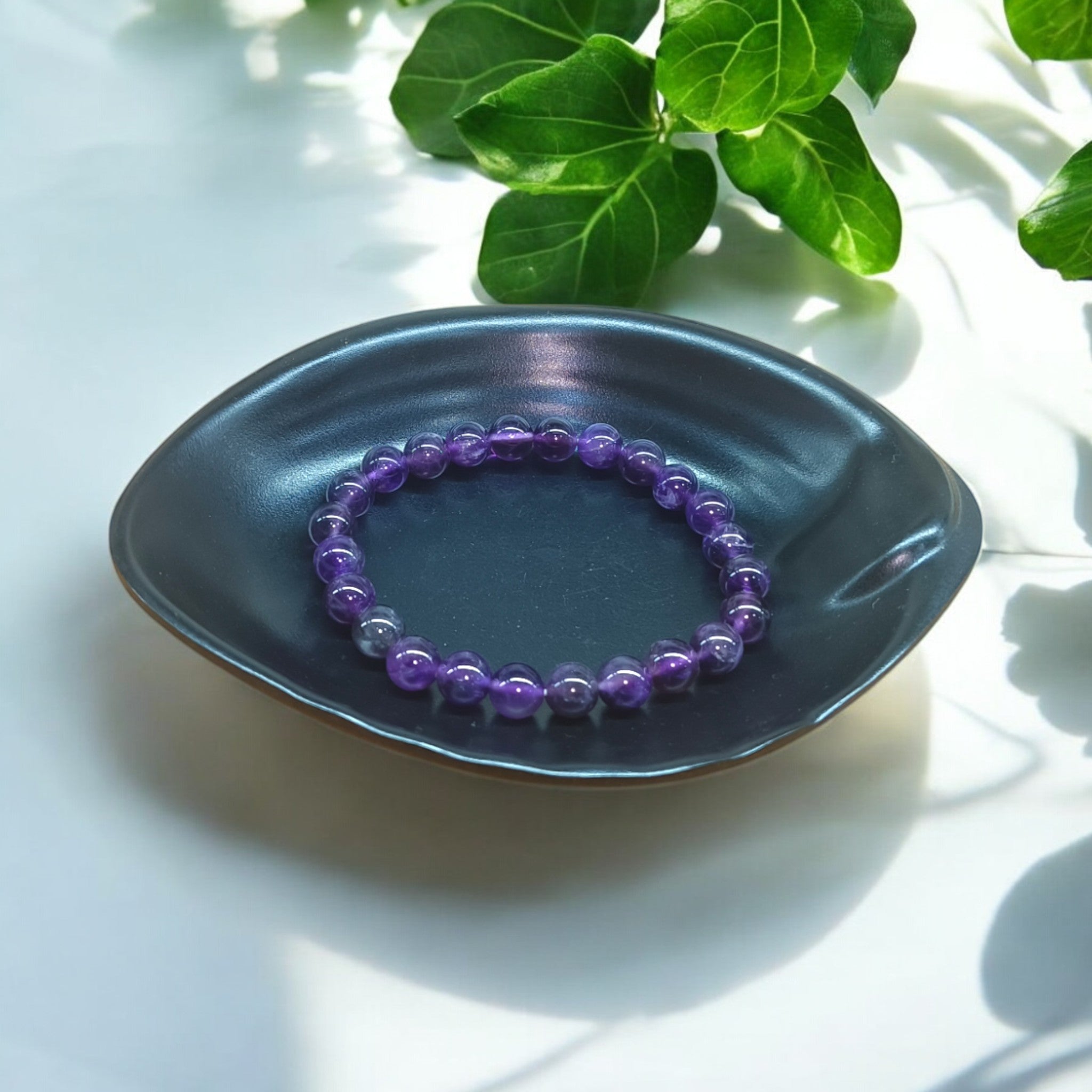 "Natural Amethyst elastic bracelet with 8 mm purple beads on Black dish and green leaves in background – crystal jewellery for calm and clarity" 