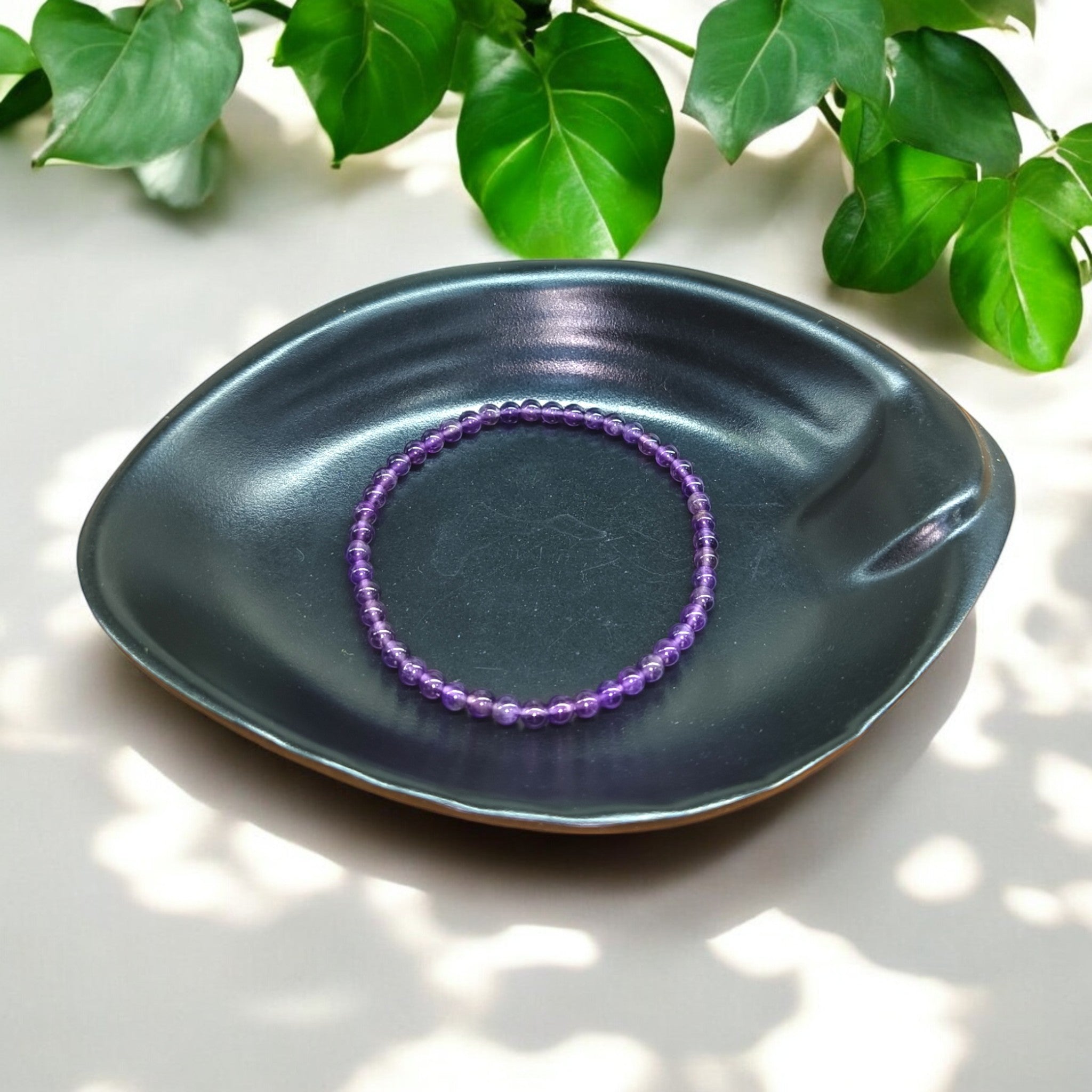 "Natural Amethyst elastic bracelet with 4 mm purple beads on Black dish and green leaves in background – crystal jewelry for calm and clarity" 