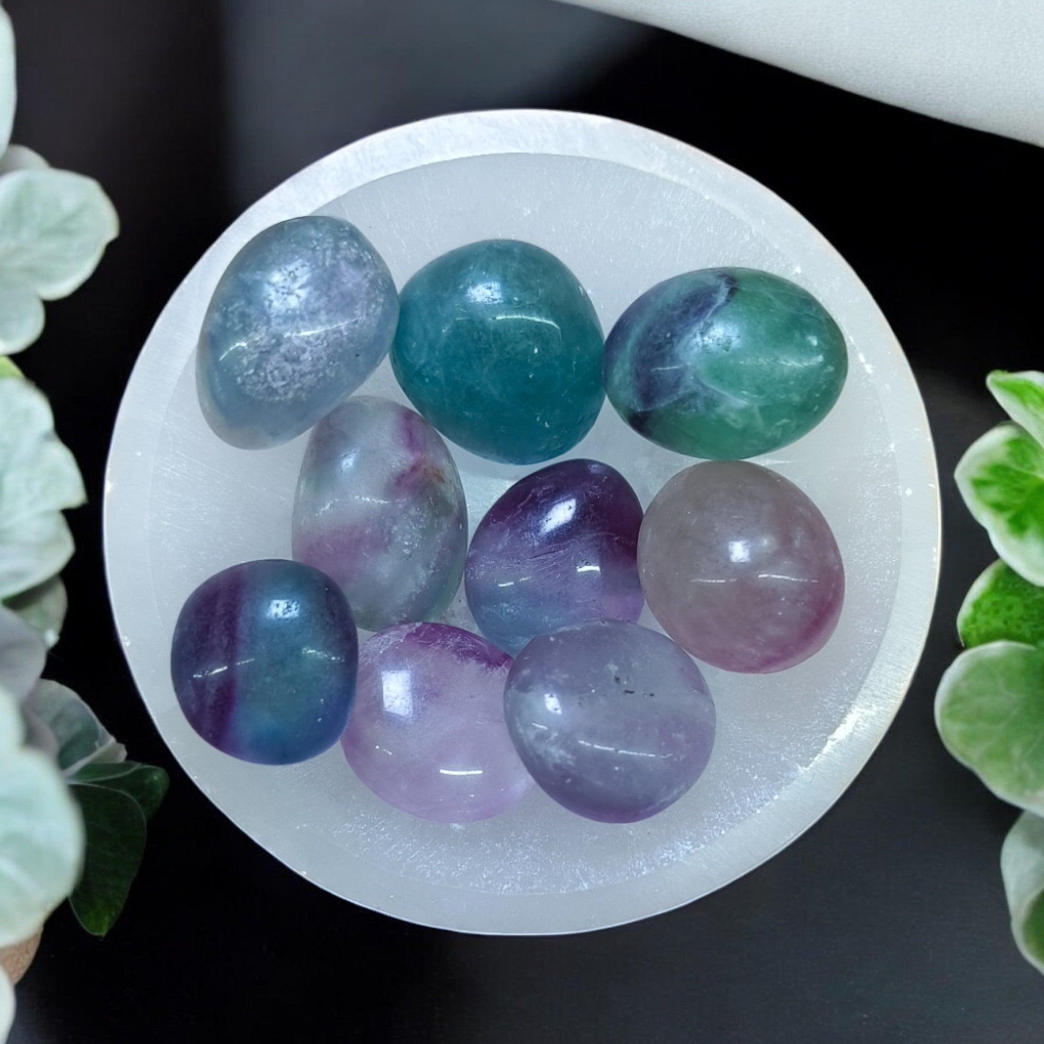 A collection of multicolored fluorite massage stones arranged on a white surface, with green and purple hues visible.