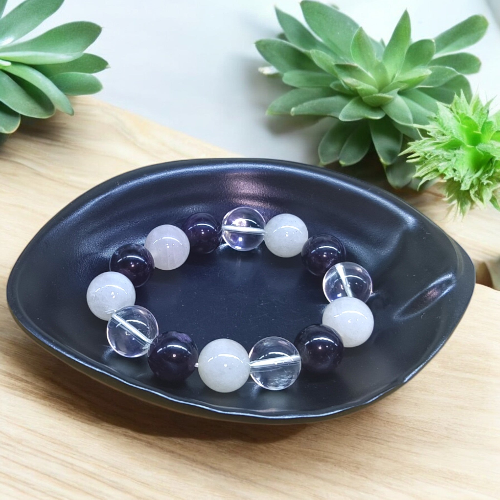 “Rose Quartz, Clear Quartz and Amethyst bracelet in 14 mm natural beads – pastel crystal trio bracelet in black dish and green leaves in background"