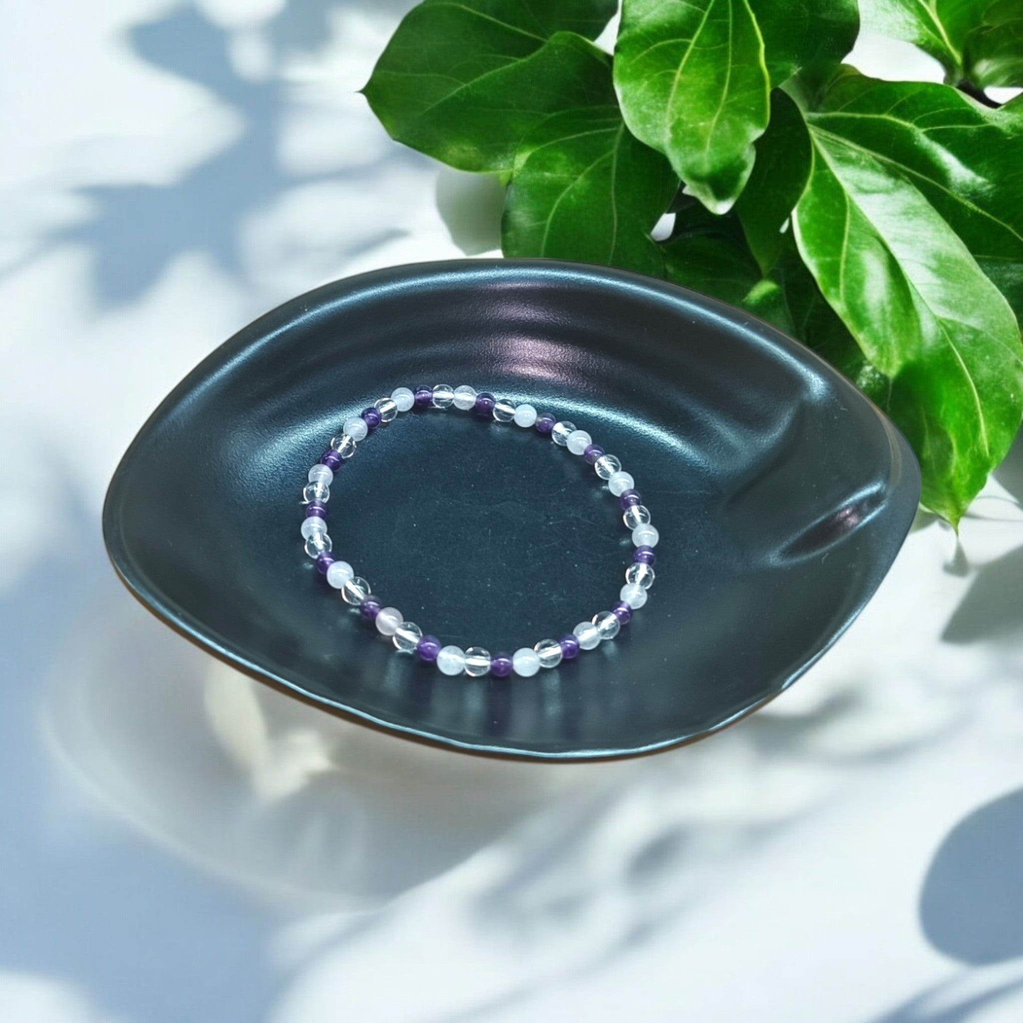 “Rose Quartz, Clear Quartz and Amethyst bracelet in 4 mm natural beads – pastel crystal trio bracelet in black dish and green leaves in background"