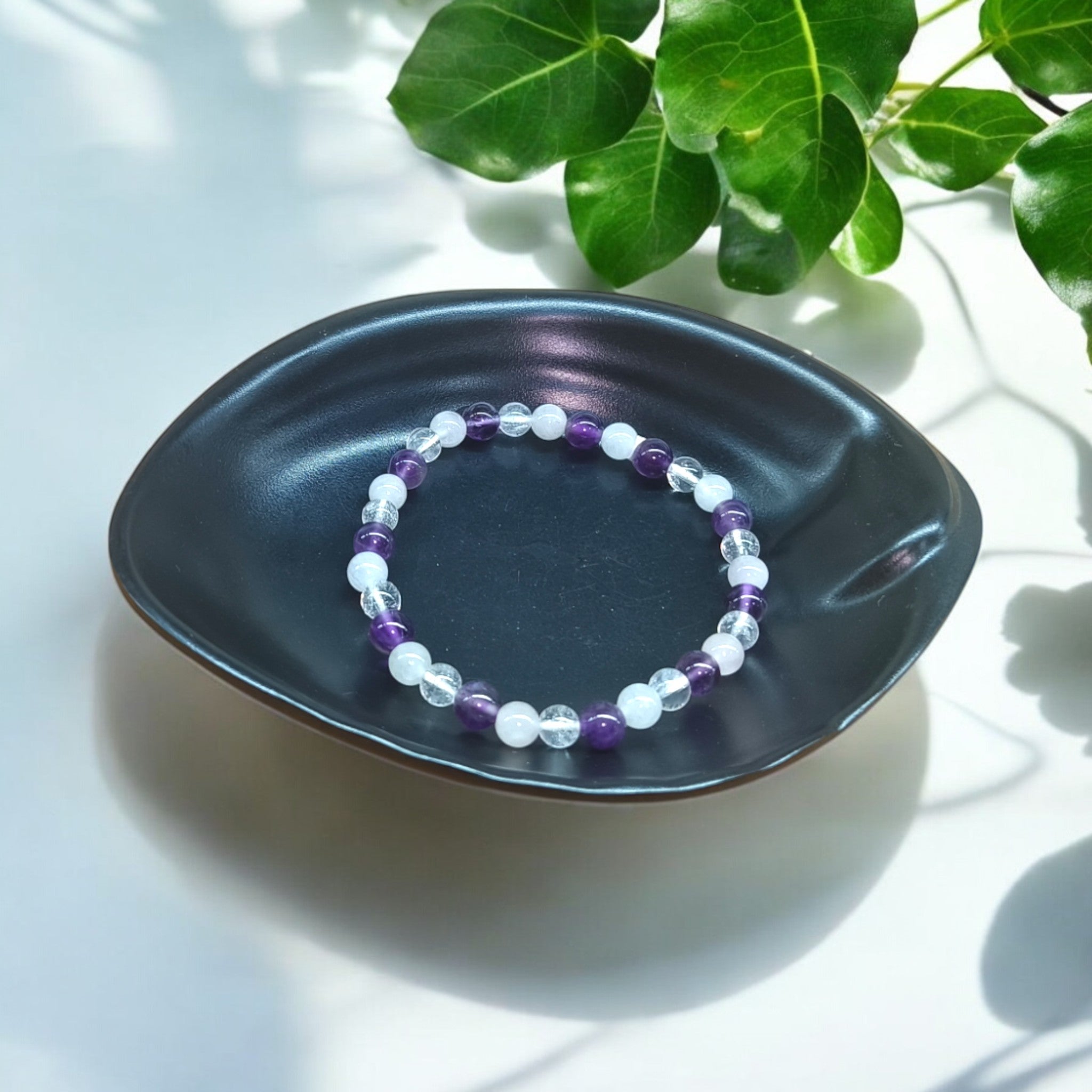 “Rose Quartz, Clear Quartz and Amethyst bracelet in 6 mm natural beads – pastel crystal trio bracelet in black dish and green leaves in background"