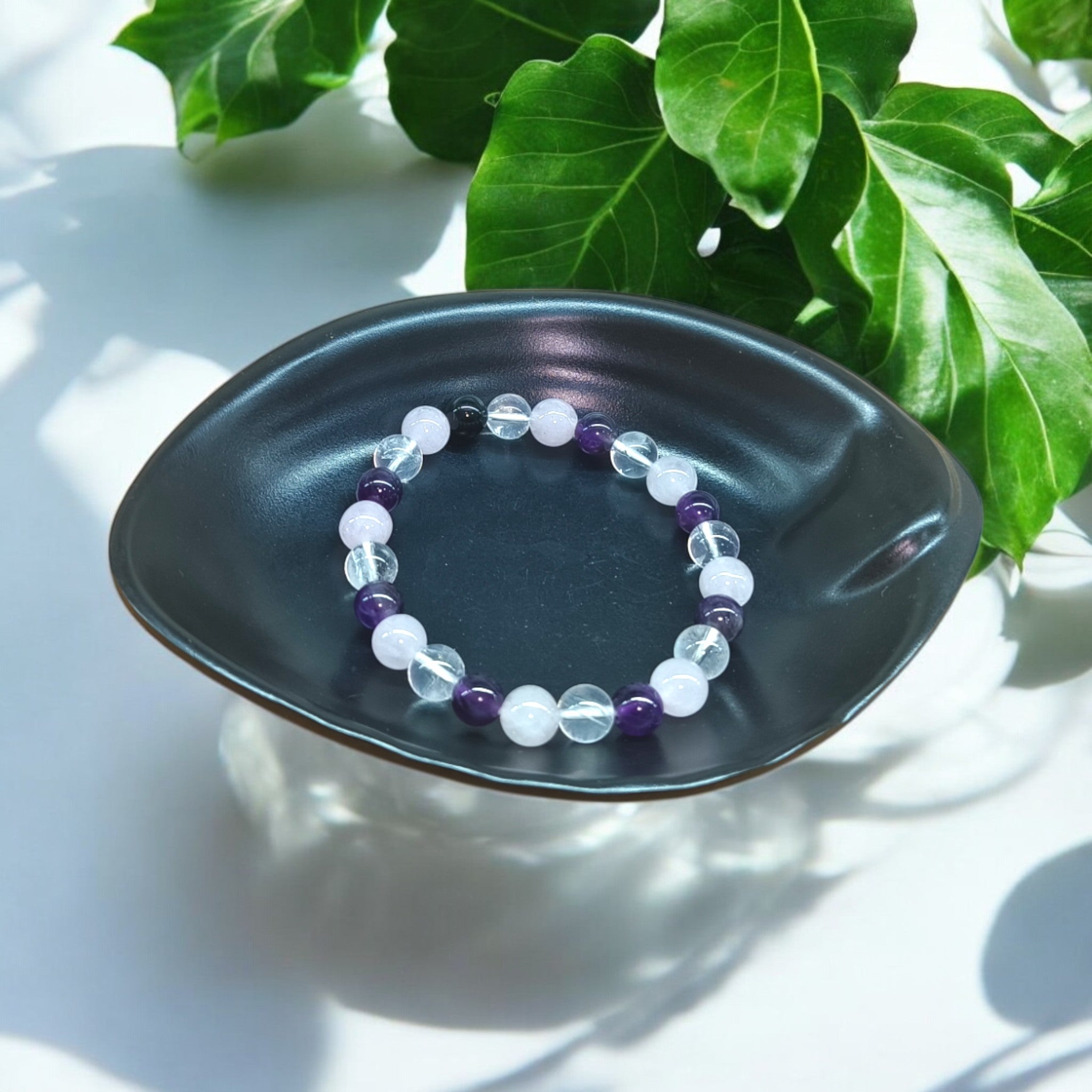 “Rose Quartz, Clear Quartz and Amethyst bracelet in 8 mm natural beads – pastel crystal trio bracelet in black dish and green leaves in background"