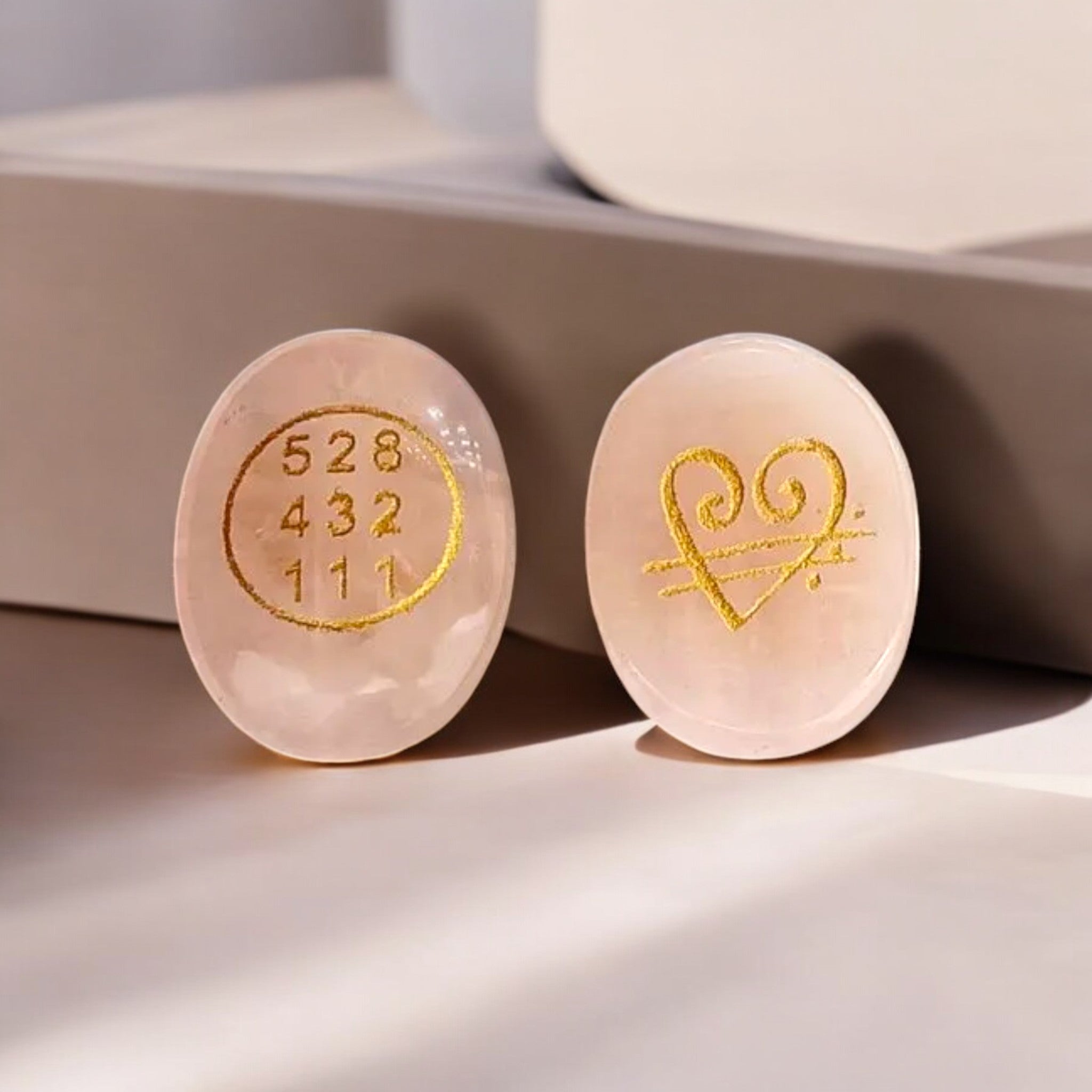 Rose quartz stones with gold embossed numbers and heart design showing front and back of the same stone  on a light background 